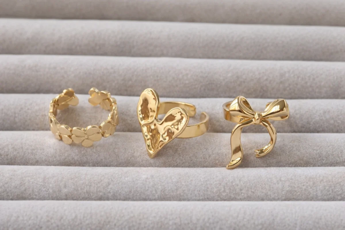 Close up of a woman's hand wearing multiple 18k gold plated rings including an engagement style solitaire.